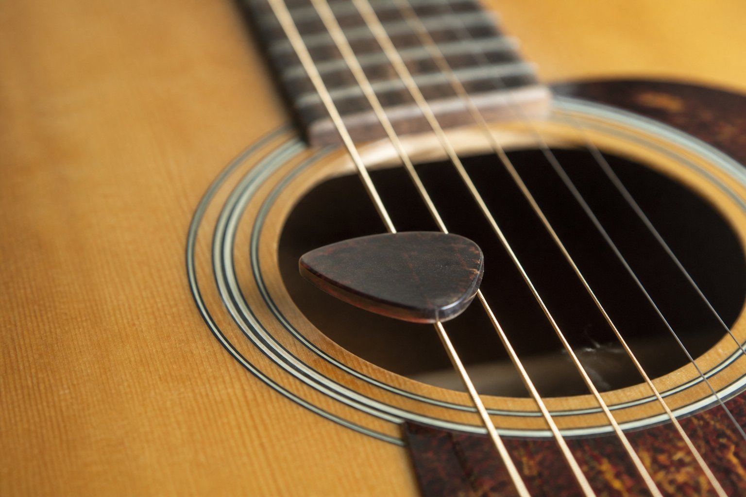 A thick plectrum resting across the strings of a dreadnought guitar just in front of the soundhole