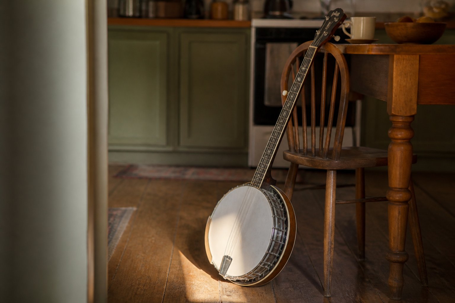 An open back five string banjo resting against a kitchen chair, late afternoon light across the head